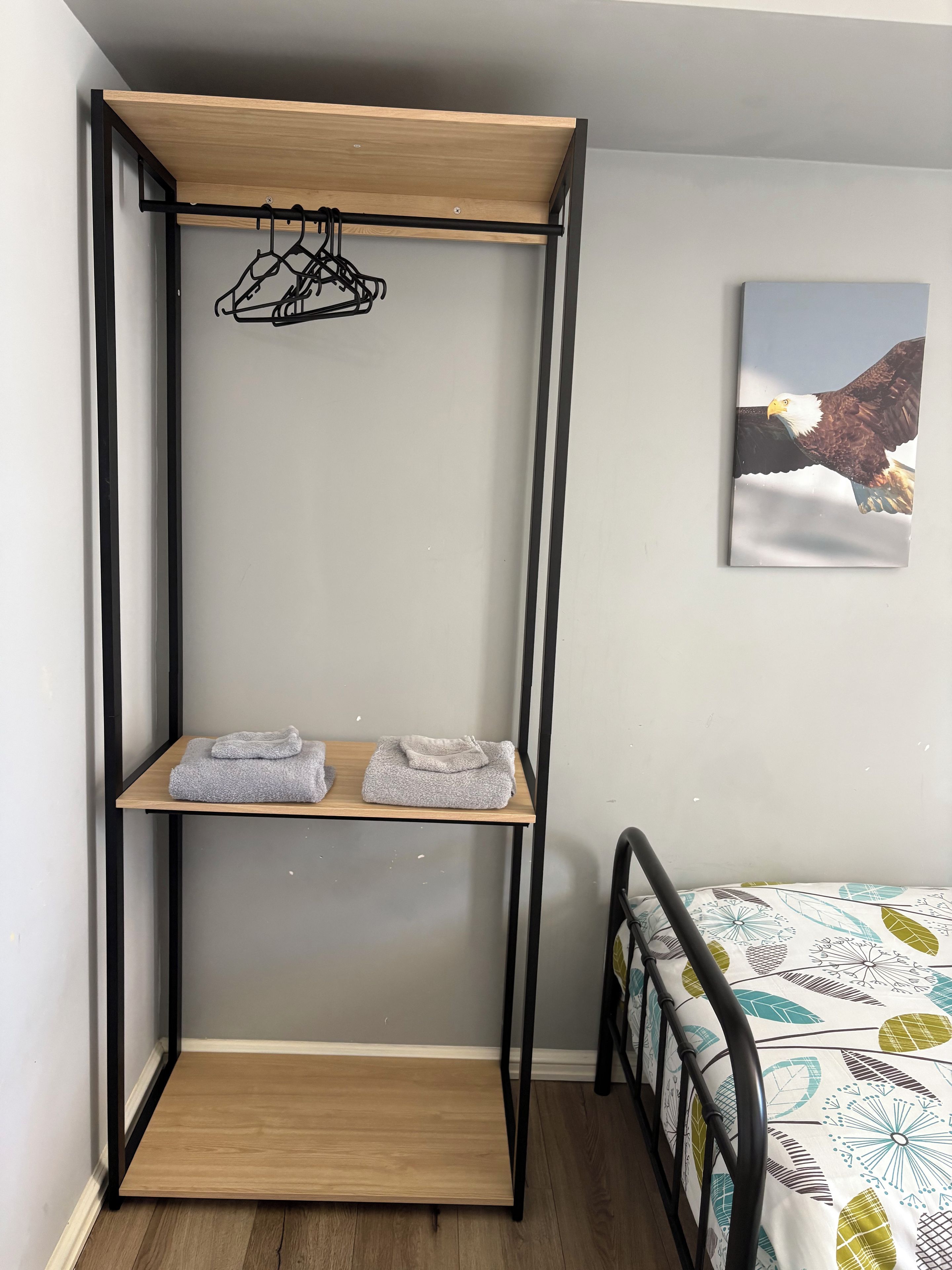 Une chambre avec un lit, une étagère en bois où sont rangées des serviettes et un tableau encadré au mur.