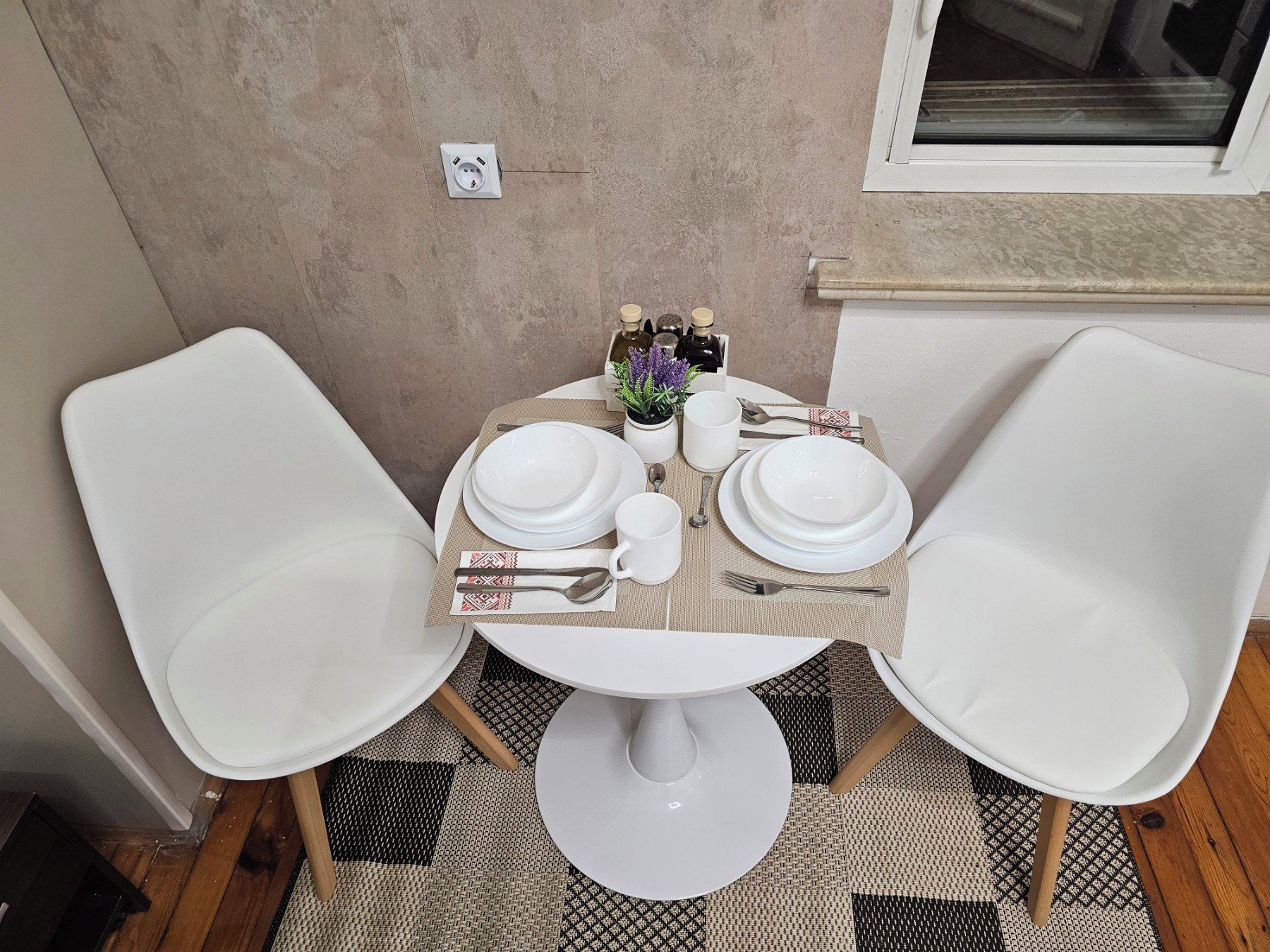 Uma mesa redonda pequena com cadeiras brancas, toalha de mesa branca e um conjunto de pratos, talheres e xícara, tudo em branco.