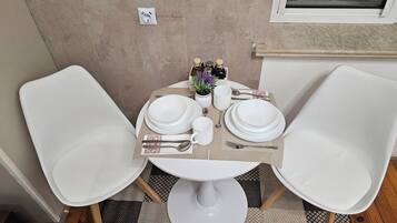 Uma mesa redonda pequena com cadeiras brancas, toalha de mesa branca e um conjunto de pratos, talheres e xícara, tudo em branco.