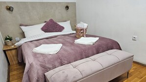 Un dormitorio con cama, una banca, una mesita de noche y un enchufe.