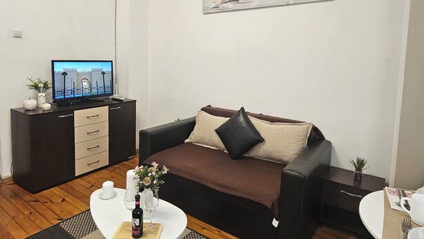 Una sala de estar con un sofá marrón, un televisor sobre un mueble negro y un cuadro de orquídeas blancas.