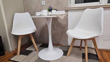 Una habitación pequeña con una mesa blanca y dos sillas blancas, una ventana y una alfombra con textura.