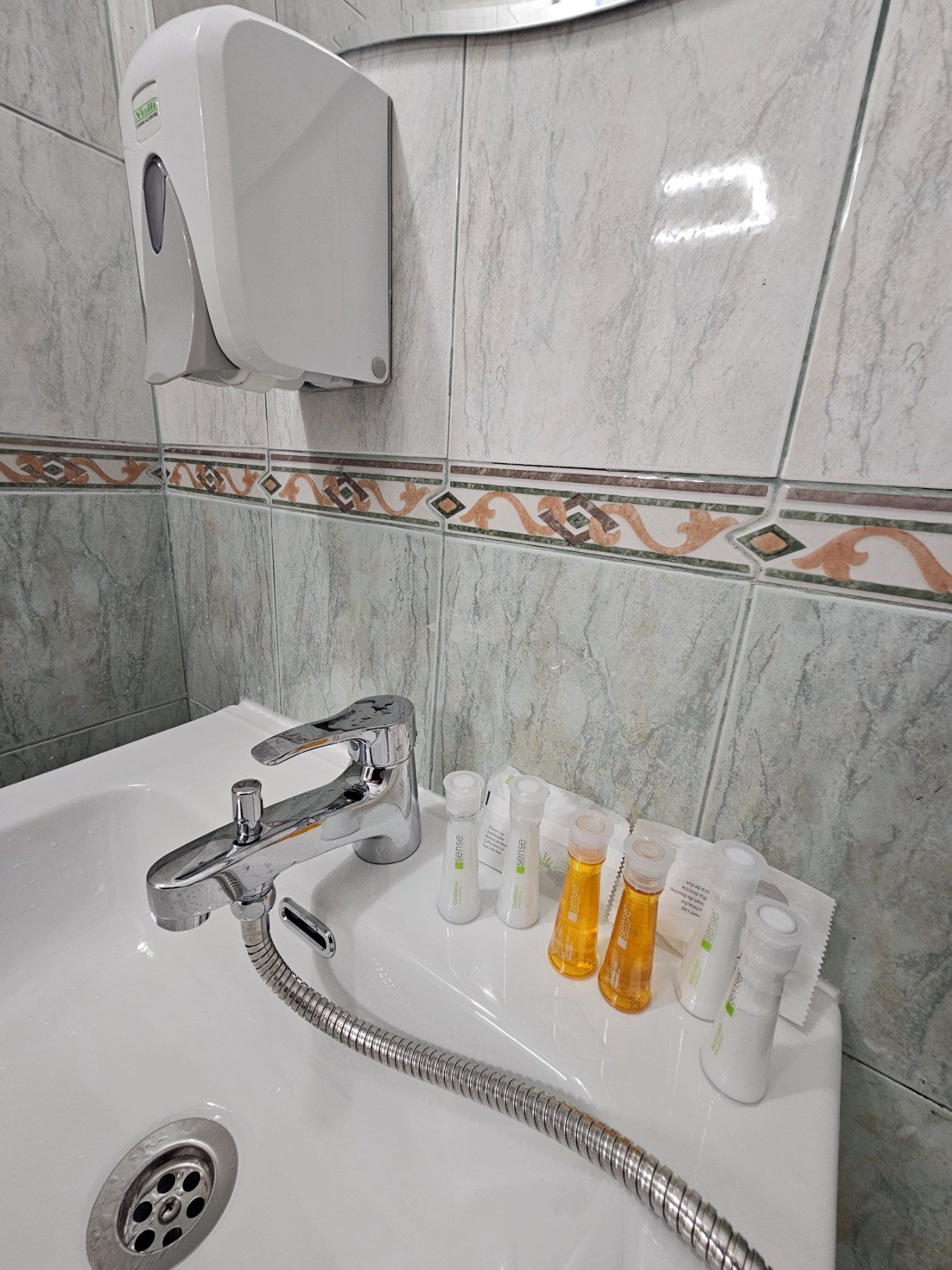 A bathroom with a white sink, chrome faucet, and a handheld showerhead. There are toiletries on the sink.