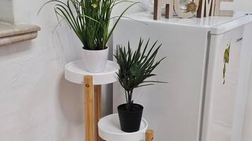 Geladeira branca com a palavra 'HOME' na parte superior, parede branca e piso de madeira.
