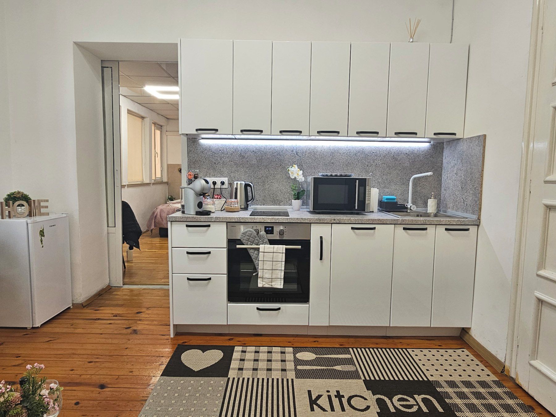 Cozinha compacta com armários brancos, micro-ondas e chaleira.