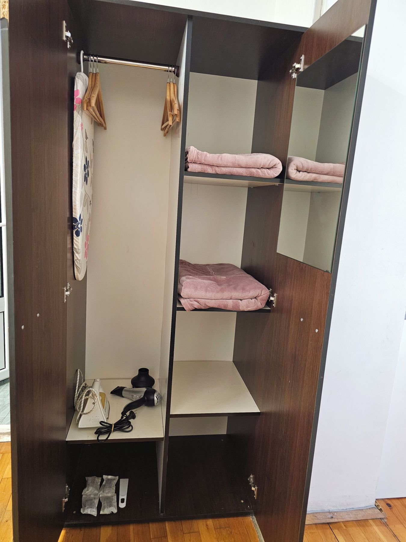 Un armario con varios estantes, una barra para colgar ropa y un compartimento inferior que contiene un secador de pelo y otros objetos.