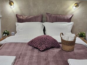 A bed with a herringbone-patterned bedspread, two white pillows, and a purple textured pillow. There is a woven basket with towels on the bed. - Apartment City center with workspace (Sofia)