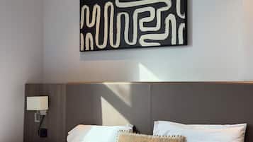 A modern hotel room with a large abstract artwork on the wall, a neatly made bed with two pillows, and a bedside table with a lamp.