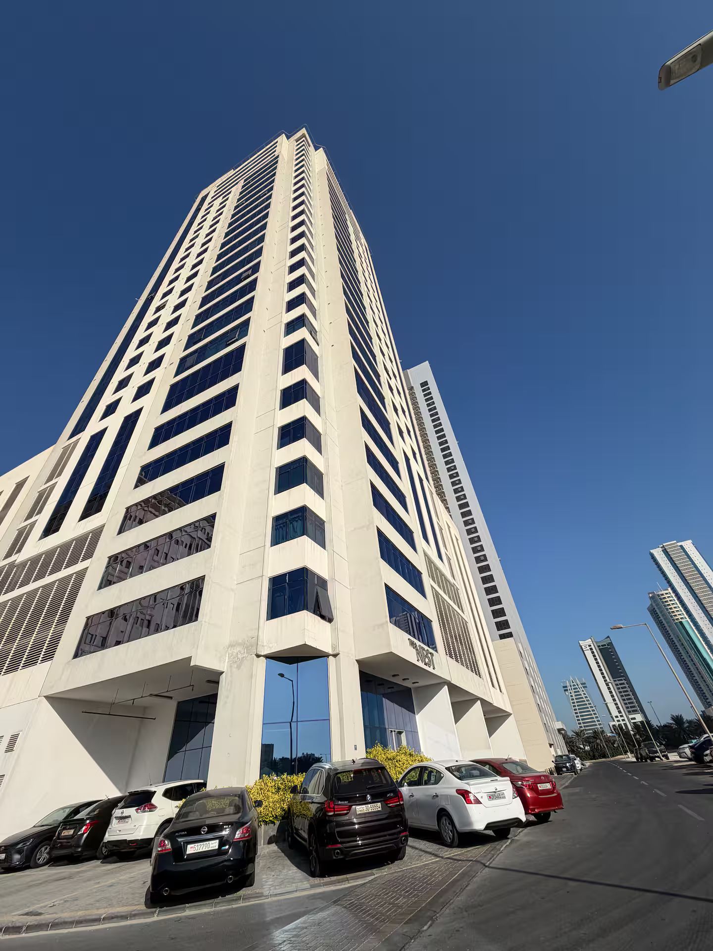 A tall, modern building with a prominent entrance and a parking lot in front.