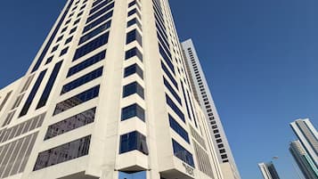 A tall, modern building with a prominent entrance and a parking lot in front.