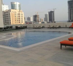 A rooftop pool with lounge chairs, surrounded by high-rise buildings and construction cranes. - Best City View Studio / Heart of the city FNS1401O (Capital Governorate)