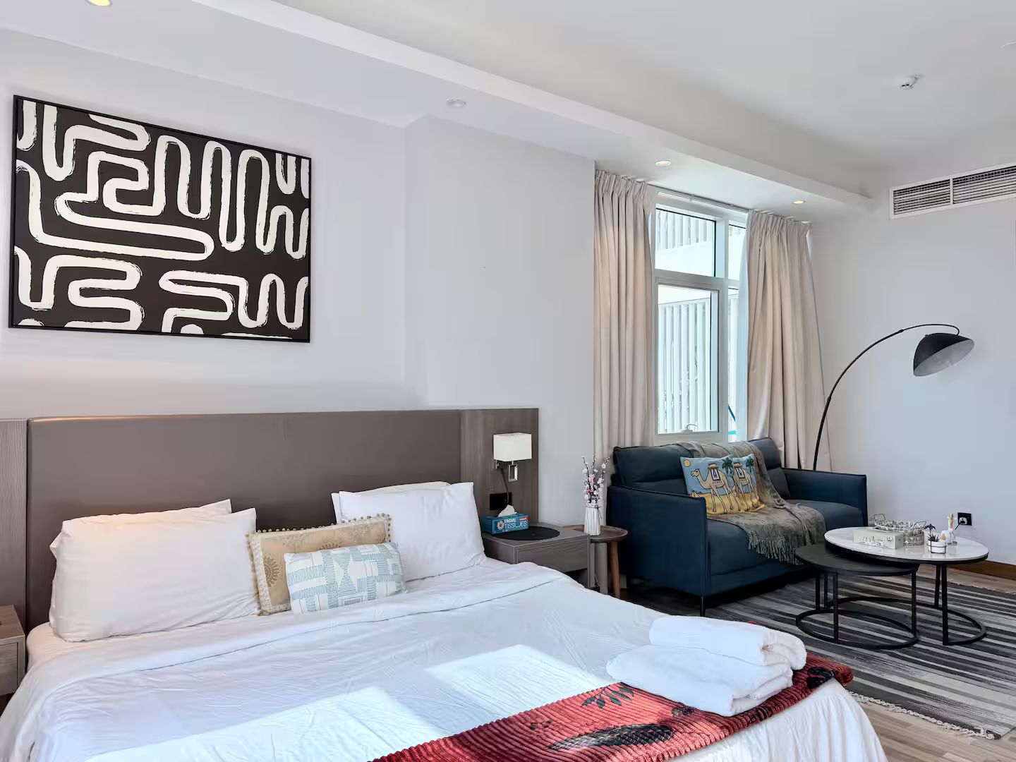 A modern hotel room with a large bed, a sofa, a small table, and a floor lamp.