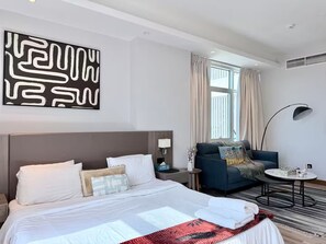 Ein modernes Hotelzimmer mit einem großen Bett, einer Couch, einem kleinen Tisch und einer Stehlampe.