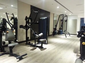 Ein Fitnessstudio mit verschiedenen Trainingsgeräten, einer Spiegelwand und einem Holzboden.
