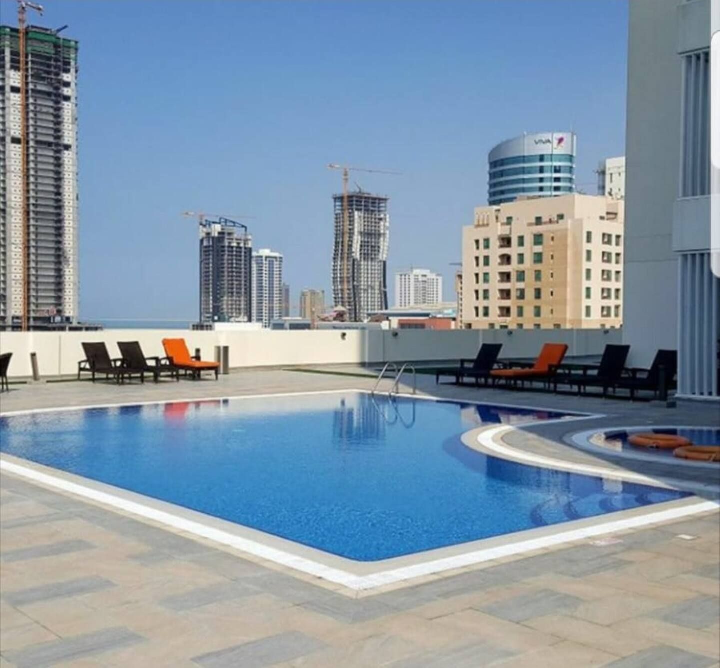 A rooftop swimming pool with lounge chairs and a view of surrounding high-rise buildings.