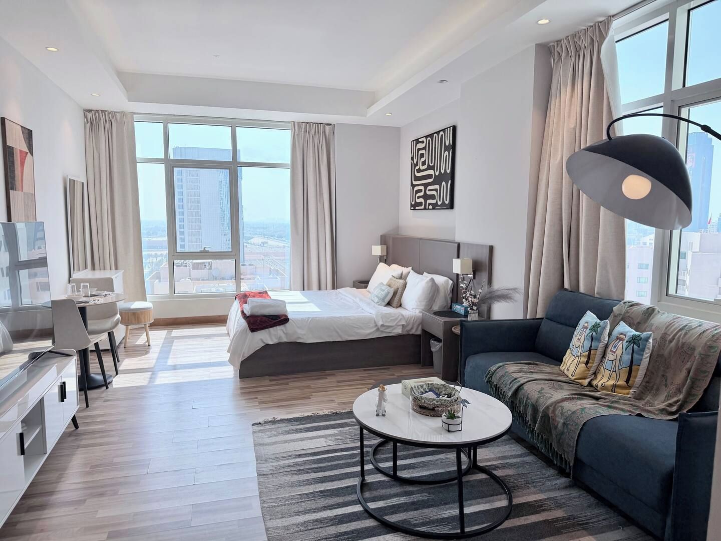 A modern hotel room with a large bed, a sofa, a dining area, and a view of the city.