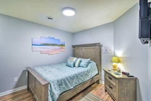 Ein Schlafzimmer mit einem Bett, einem Nachttisch, einer Lampe und einem an der Wand befestigten Fernseher.