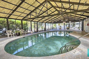 An indoor swimming pool with a covered roof, clear glass walls, and a few chairs and potted plants around the pool area. - Your Beach Escape – Close to Cherry Grove Beach (Little River)