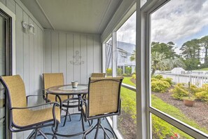 A covered patio with a round table and four chairs, a view of a house and garden through the glass doors. - Your Beach Escape – Close to Cherry Grove Beach (Little River)