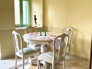 Ein Essbereich mit einem runden Tisch, weißen Stühlen und einer Tischdecke mit Blumenmuster.