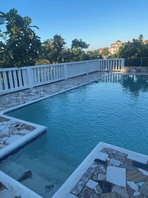 A swimming pool with a white fence and tiled edges, surrounded by trees and a building in the background. - Peaceful, private 2-bedroom house with exclusive pool in Montego Bay (Montego Bay)