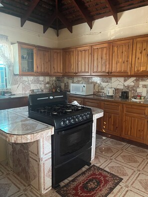 A kitchen with wooden cabinets, a gas stove, a microwave, and a tiled backsplash. - Peaceful, private 2-bedroom house with exclusive pool in Montego Bay (Montego Bay)