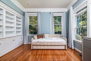 Quarto com cama grande, estantes embutidas e vista para árvores pelas janelas.