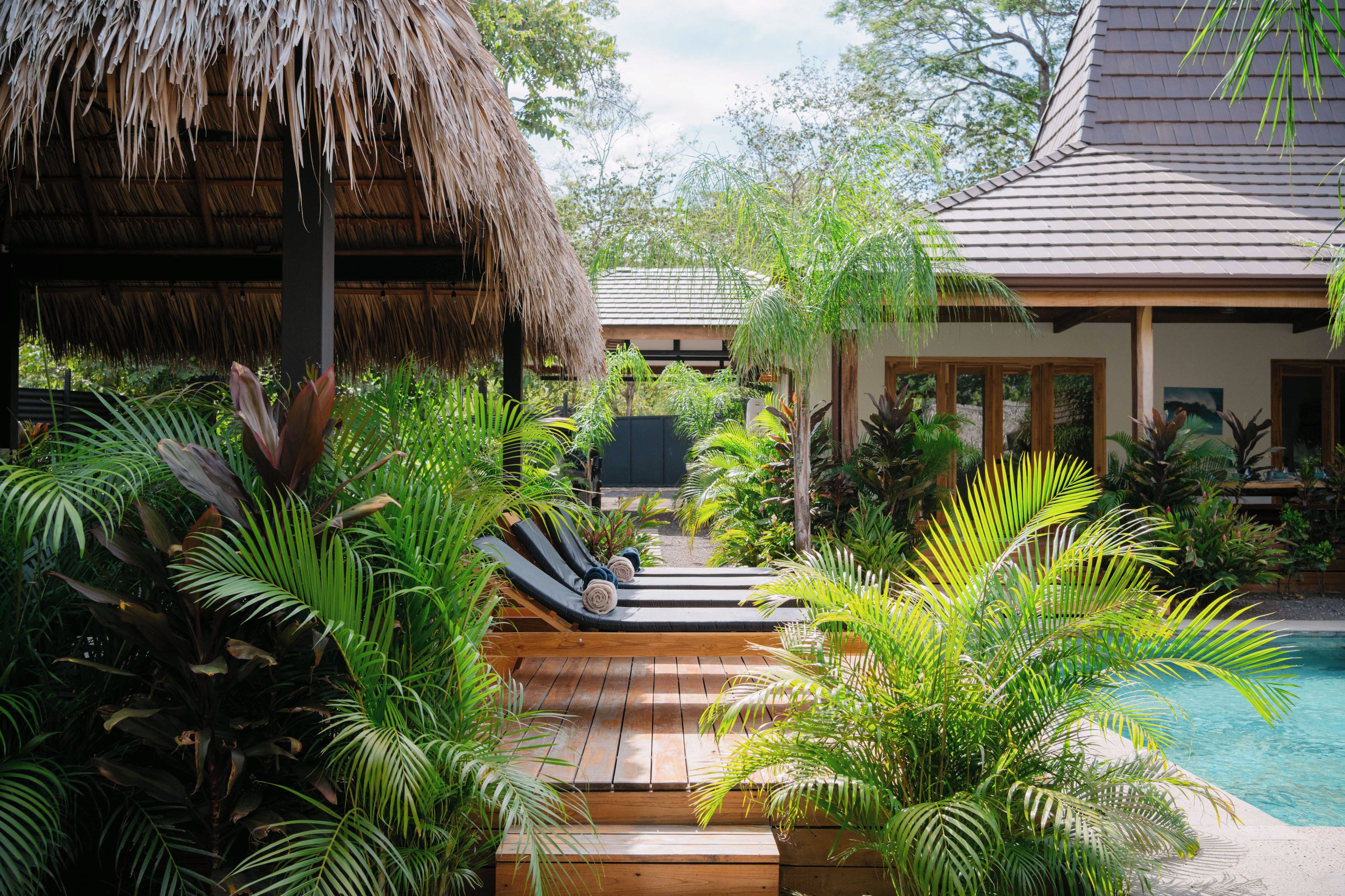 Ein tropisches Resort mit Pool, Holzterrasse und üppiger Vegetation.