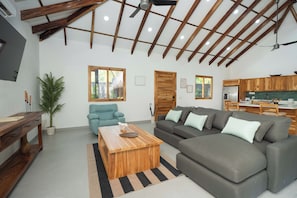 A modern living room with a sofa, coffee table, and a dining area with a kitchen in the background. - Casa Moana l Luxury Balinese Villa- AC-Golf Cart (Playa Avellanas)