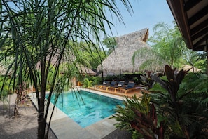 A pool area with lounge chairs and a thatched-roof structure. - Casa Moana l Luxury Balinese Villa- AC-Golf Cart (Playa Avellanas)