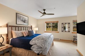 Ein Schlafzimmer mit einem Bett, einem Deckenventilator, einem Fenster und einem an der Wand montierten Fernseher.