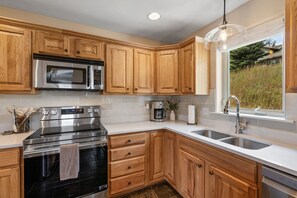 A modern kitchen with wooden cabinets, stainless steel appliances, a built-in oven, a microwave, a coffee maker, and a window with a view of the outdoors. - *New!* Big Sky Basecamp | Town Center & Hot Tub (Big Sky)