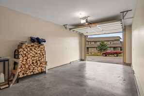 Eine Garage mit Betonboden, einem Holzstapel und einem roten Fahrzeug davor.