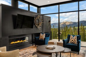 Ein modernes Wohnzimmer mit Kamin, großen Fenstern und Blick auf die Berge.