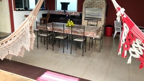 A dining area with a table set for six, surrounded by chairs, a hammock, and a red trash bin. - BEAUTIFUL HOUSE IN GATED COMMUNITY (Itupeva)