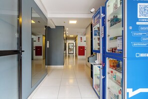 A corridor with a blue pharmacy display, glass doors, and emergency exit signs. - Aquarela by Bhomy  (São Paulo)