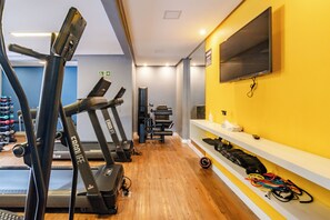 Un gimnasio con cintas de correr, pesas y un televisor en la pared.