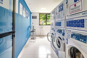 A laundry facility with multiple washing machines, instructional posters, and a window providing natural light. - Aquarela by Bhomy  (São Paulo)