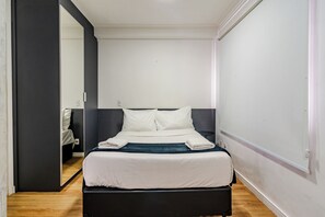 Habitación de hotel con una cama individual, una mesita de noche, un espejo y una puerta que da a otra habitación.