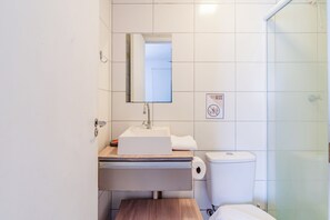 Un baño con lavamanos blanco, espejo, inodoro y ducha.