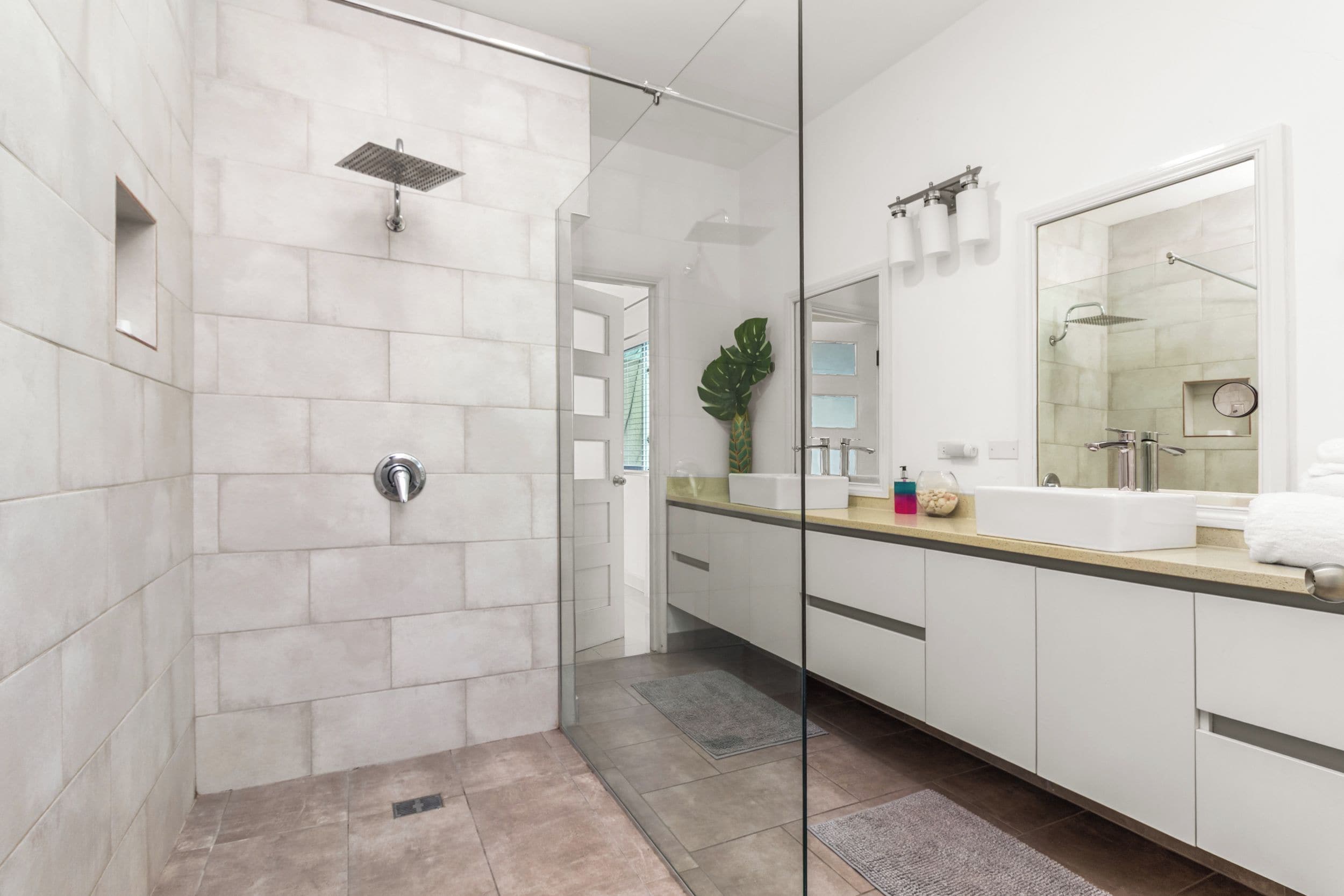 Un baño moderno con ducha de vidrio, un espejo grande y un tocador con lavamanos.