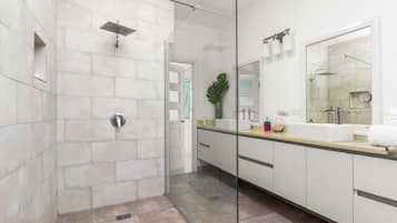 Un baño moderno con ducha de vidrio, un espejo grande y un tocador con lavamanos.