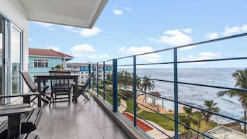 Un balcón con vistas al mar, una mesa de comedor con sillas y un edificio de fachada azul.