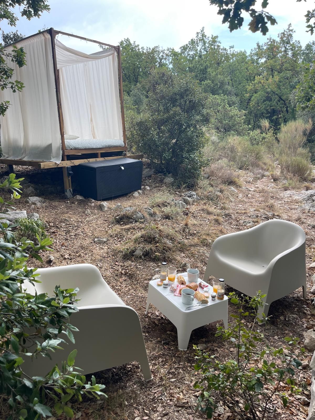 Een tent met een luifel, een klein tafeltje met ontbijtartikelen en twee stoelen in een natuurlijke omgeving.