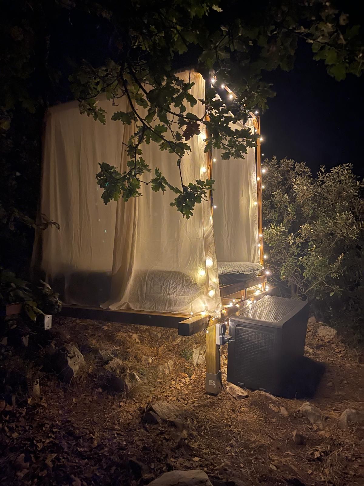 A tent-like structure with a canopy, surrounded by trees and illuminated by string lights.