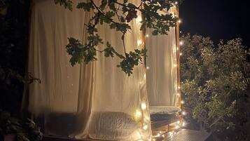 A tent-like structure with a canopy, surrounded by trees and illuminated by string lights.
