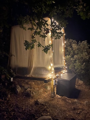 Une structure en forme de tente, dotée d’un auvent, entourée d’arbres et illuminée par des guirlandes lumineuses.