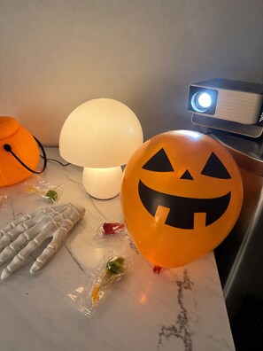 A room with a white lamp, a projector, and Halloween-themed decorations including a jack-o'-lantern balloon. - Cozy Downtown Perpignan Apartment (Perpignan)