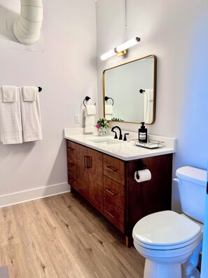 Un baño moderno con inodoro blanco, tocador de madera y un espejo grande.