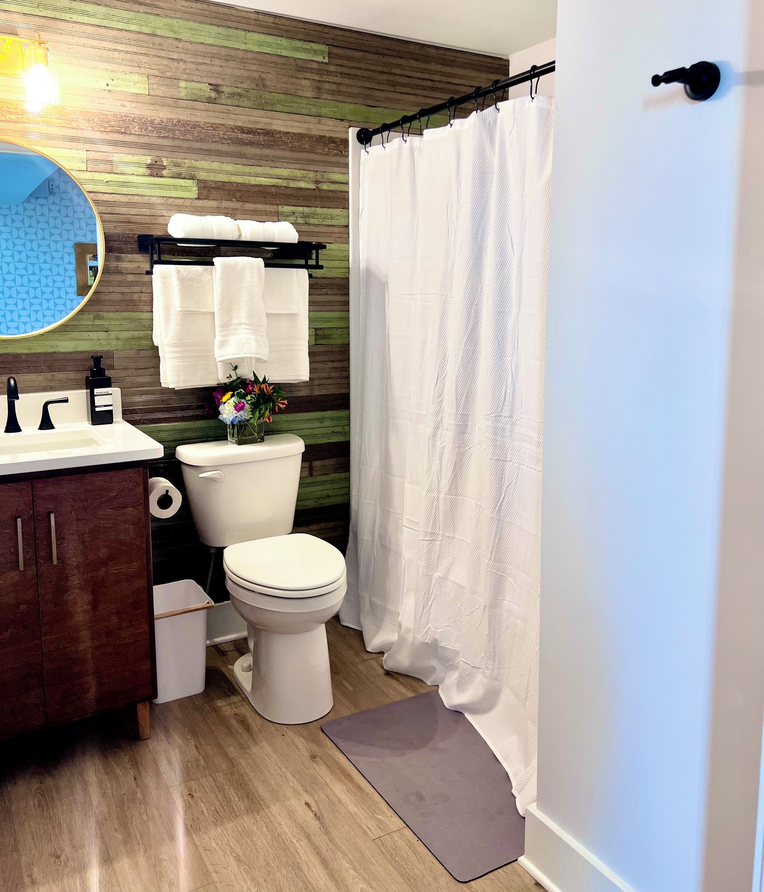 A bathroom with a wooden wall, a toilet, a sink, a mirror, and a shower curtain.